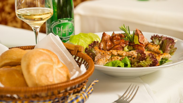 Appetizer in the Genuss.Restaurant, © Rita Newman A plate of salad and meat, a basket of bread and a glass of white wine on a table.