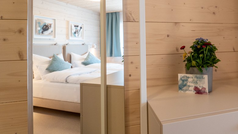 Cozy ambience, © freilich / IsaBella Fritsche A cozy bedroom with wooden walls, a bed with blue pillows and a small table with a plant and a map.