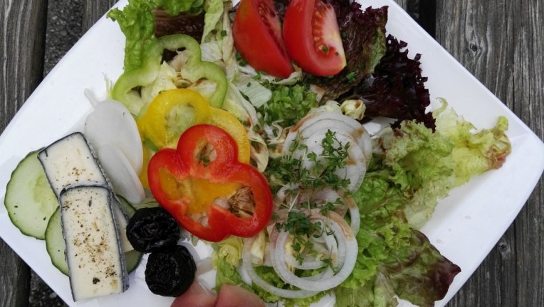 Heurigen snack, © Weinberghof Ilkerl A plate of lettuce, tomatoes, peppers, onions, ham and cheese on a wooden table.