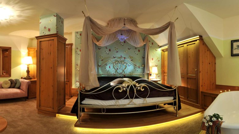 Fantasia themed suite, © Hotel Donauterrasse A luxurious bedroom with four-poster bed, wooden furniture and bathtub.