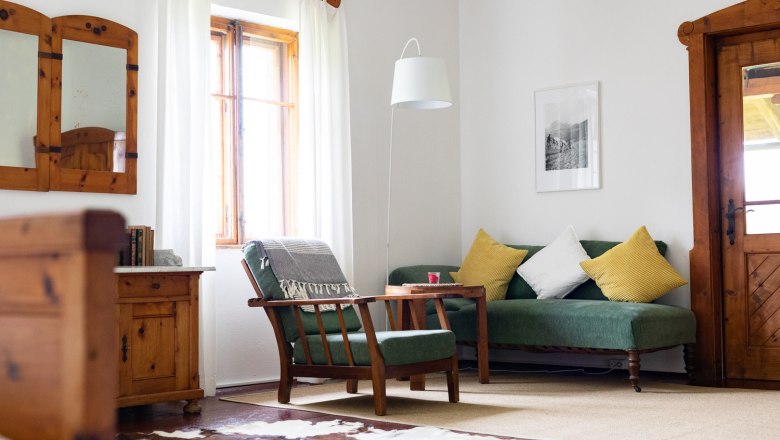 Special summer freshness flair in the rooms, © Wiener Alpen - Lierzer Cozy living room with wooden furniture, green sofa, yellow cushions and cowhide carpet.