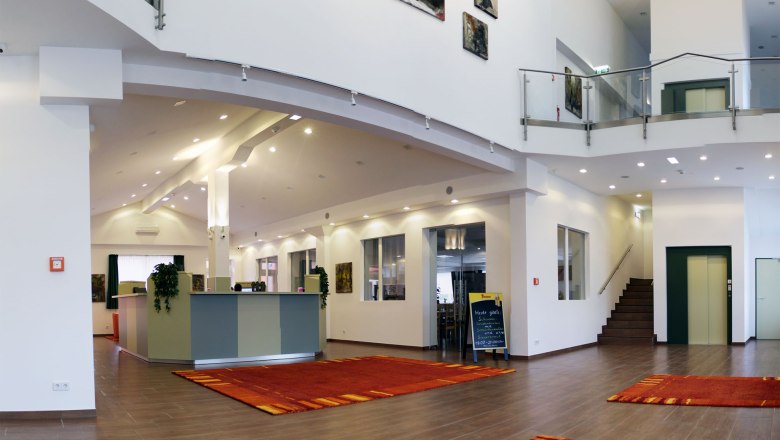 winrooms-03, © Winrooms Betriebs GmbH Modern hotel lobby with reception, red carpets and works of art on the walls.