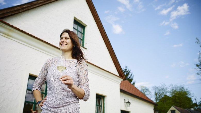Winemaker Agnes Lehner-Minkowitsch, © Alexander Bernold Woman with a wine glass in front of a white house with a red roof.
