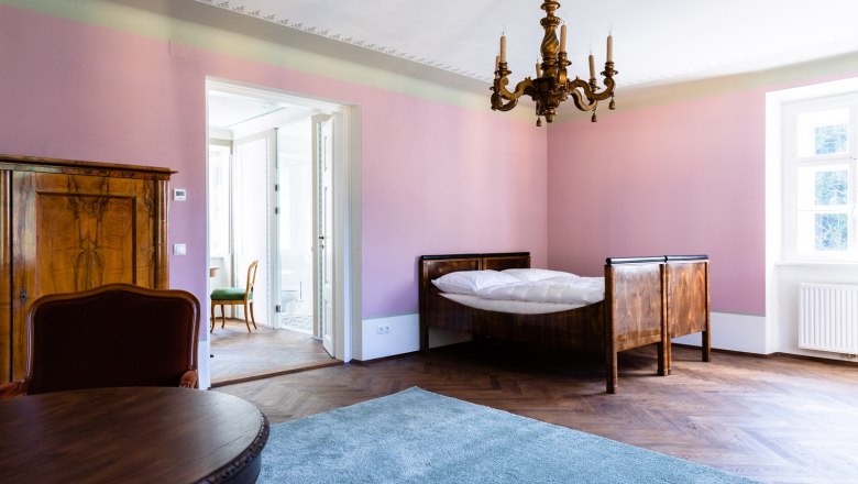 Room, © Thalhof, Katrin Nusterer An elegant room with pink walls, a wooden bed, a chandelier and a carpet on a wooden floor.