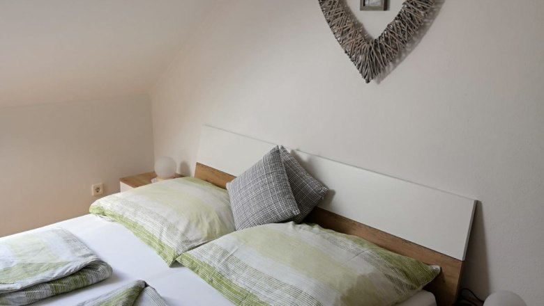 Room 2, © Haselberger Bedroom with double bed, green bed linen and heart-shaped wall decoration.