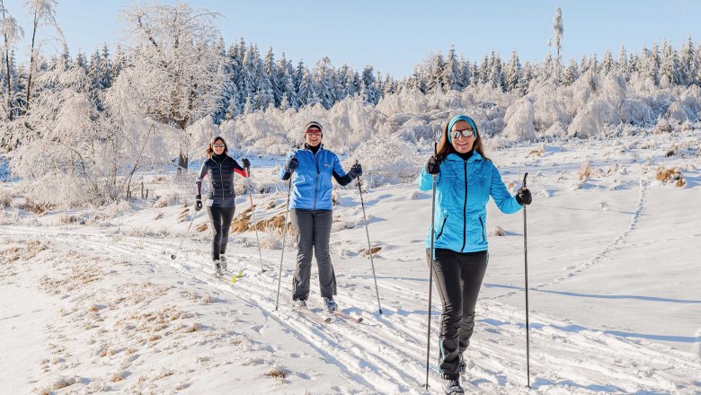 Cross-country skiing on the Nebelstein, © Christian Freitag Three people cross-country skiing in the snow with snow-covered trees in the background.