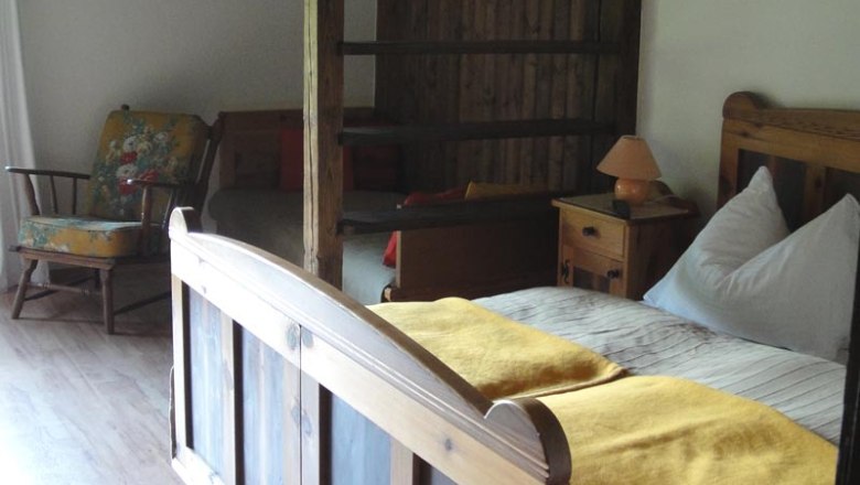 Farmhouse parlor room, © Familie Kellner Rustic room with wooden bed, yellow ceiling, rocking chair and wooden walls.