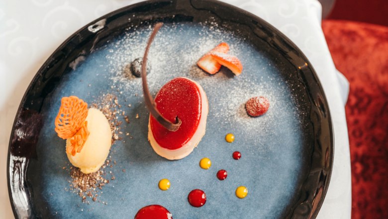 Ruby cocoa bean mousse tartlets with calamansi sorbet, © Niederösterreich Werbung/Daniela Führer An artfully arranged dessert on a blue plate with red and yellow sauce dots.