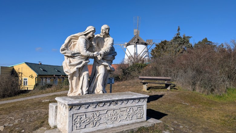 Calvary, © Retzer Land / Daniel Wöhrer Stone sculpture on a hill with a windmill in the background.