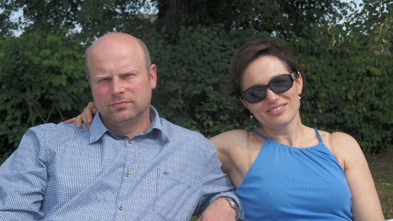 Gerald and Angelika, © Neumayr A man and a woman are sitting next to each other outdoors, the woman is wearing sunglasses.