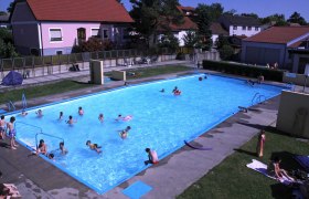 Weinbergbad Göttlesbrunn, © Gemeinde Göttlesbrunn An outdoor pool with several people in the water and on the sunbathing lawn.