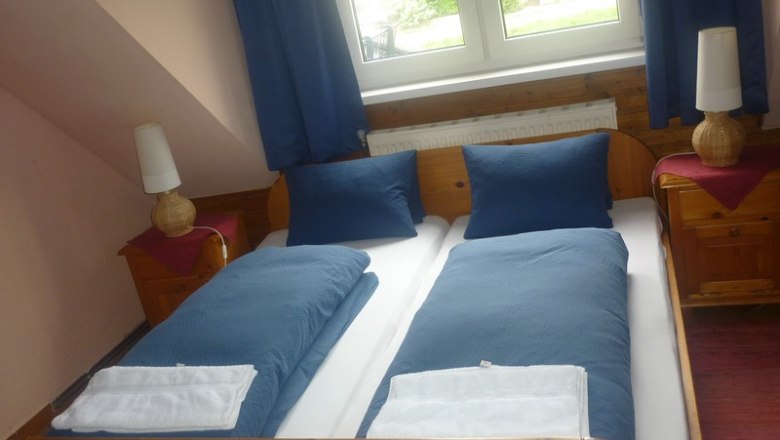 Double room, © el pirata A cozy double room with two single beds, blue bed linen and two bedside tables with lamps, under a window with blue curtains.