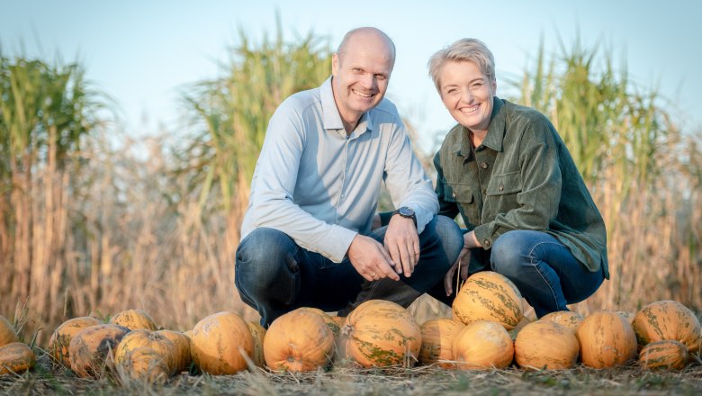 Metz pumpkin farm, © Uschi Wolf Two people kneel smiling behind a row of pumpkins in a field.