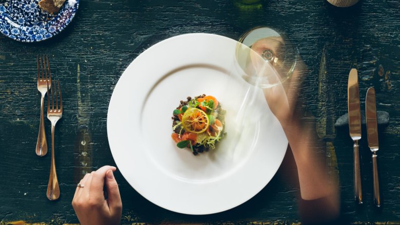 Fine food and exquisite wines, © Hofmeisterei Hirtzberger/Julius Hirtzberger A plate with an artfully arranged dish, surrounded by cutlery and a wine glass on a rustic table.