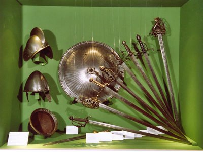 Weapons from the Anton collection, © Zwettler Musuemsverein Exhibition of antique weapons and helmets in a green display case.