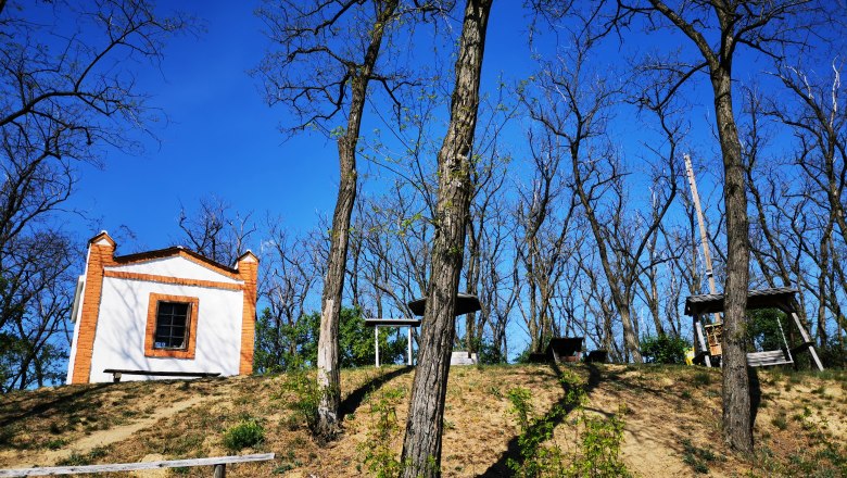 Hutberg Haugsdorf, © Weinstraße Weinviertel White building with red bricks on a hill, surrounded by bare trees under a blue sky.