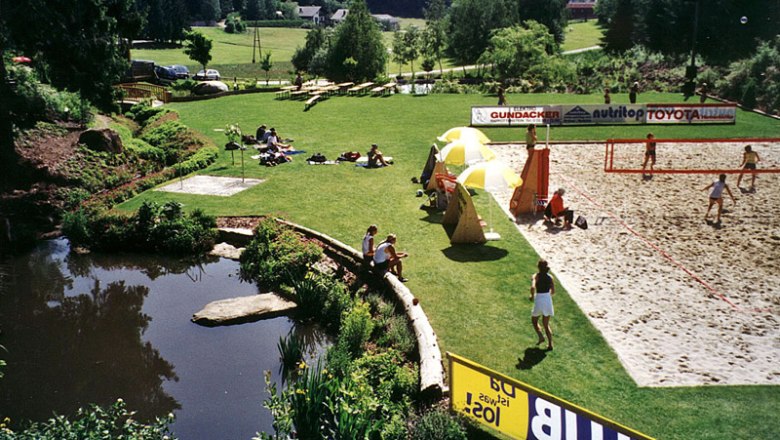Arbesbach bathing pond, © Gemeinde Arbesbach Green meadow with swimming pond, volleyball court and people relaxing and playing.