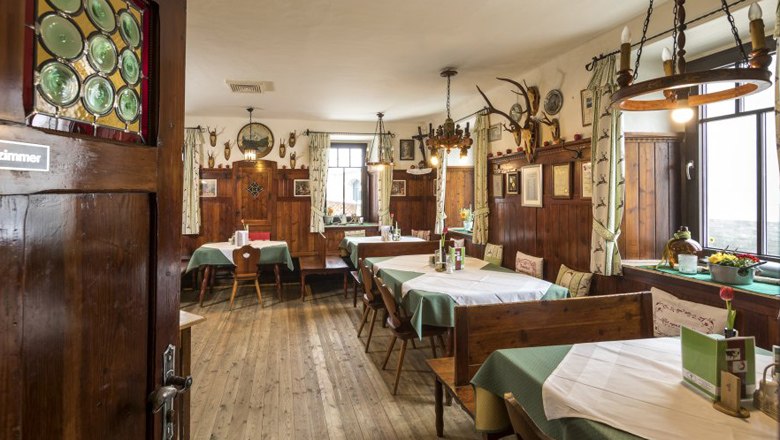 The dining room in the Grüner Baum inn, © Kurt Pinter Cozy dining room with wooden furniture, green curtains and hunting trophies on the wall.