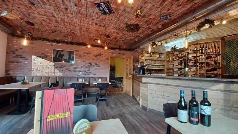 New restaurant - Wirtshaubühne Bernhart, © Wirtshausbühne Bernhart Cozy dining room with wooden tables, bar and bottles of wine.