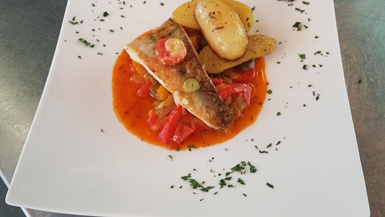 Fillet of fish, © Reef & Beef A fish fillet on a white plate, served with paprika vegetables and potatoes, garnished with herbs.