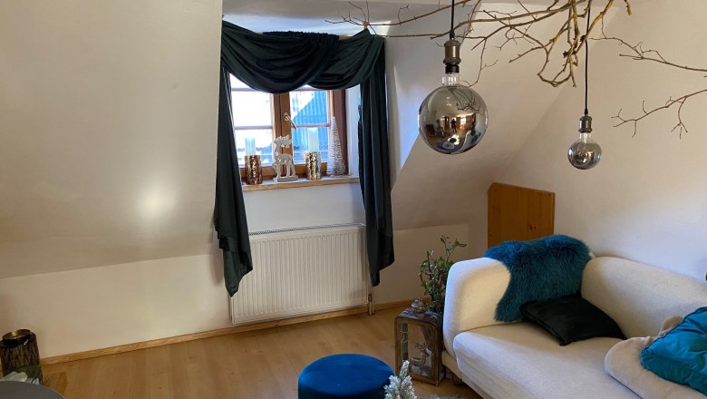 Living room, © Wiener Alpen Cozy living room with sofa, wooden floor, windows with curtains, decorative candles and hanging lamps.