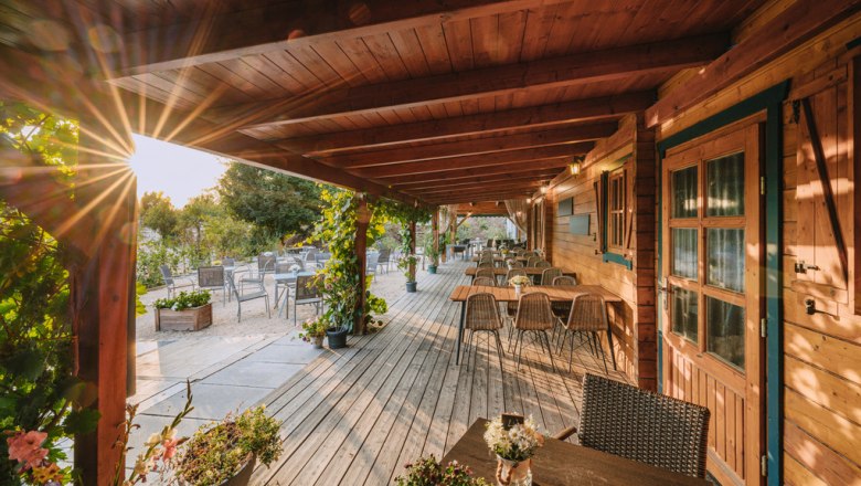 Wonderful terrace to enjoy - Weinviertler wine tavern, © Martin Mathes Wooden terrace with tables and chairs, surrounded by plants, at sunset.