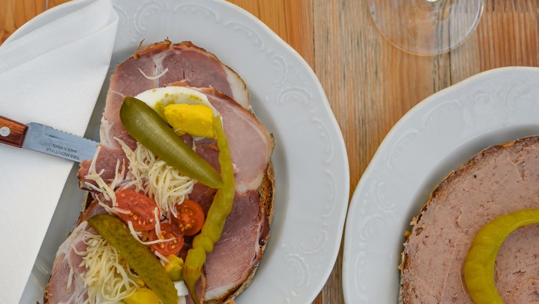 Heurigen snack, © Weinviertel Tourismus GmbH / Lisa Sedlatschek Two plates with sandwiches and two glasses of white wine on a wooden table.