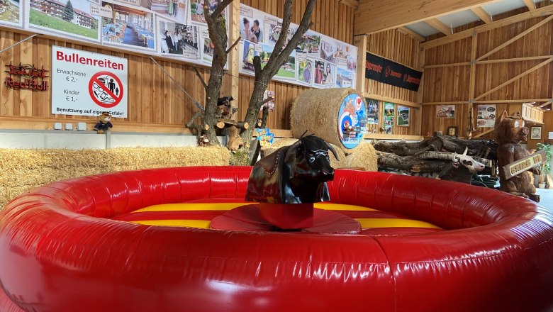 Bull riding, © Wiener Alpen Inflatable bull riding facility in a wooden hut with decorations and signs.