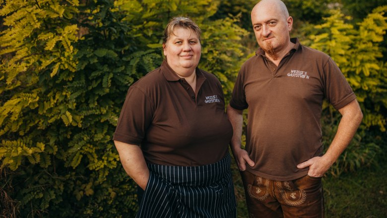 Petra and Andreas Weissenböck, © Niederösterreich Werbung/Daniela Führer Two people in brown polo shirts in front of green bushes.