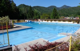 Hohenberg alpine spa, © Marktgemeinde Hohenberg An empty outdoor pool with blue water, surrounded by mountains and trees.