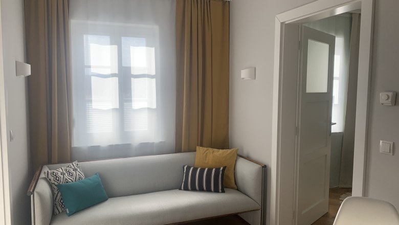 Apartment 1 "It's so cozy", © kremsoase Cozy living room with sofa and cushions, yellow curtains and open door frame.