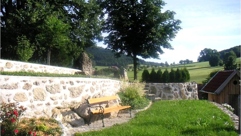 EXPERIENCE: Stone & Garden, © Familie Anderl A garden with a stone wall, bench and trees in the background.