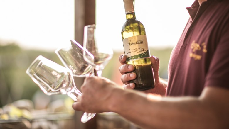 Wine tavern Oßberger, © Nino Zimmerhackl Person holding a bottle of 2016 Grüne Veltliner and several glasses of wine.