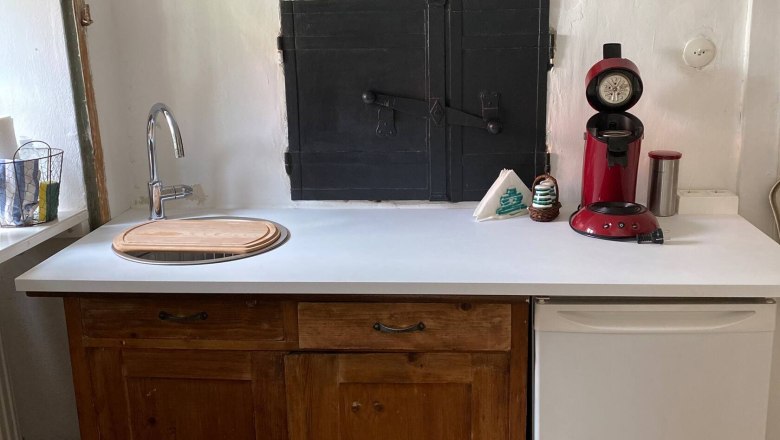 Kitchen part, © Familie Stagard Small kitchen with wooden cupboards, white worktop, red coffee machine and small fridge.