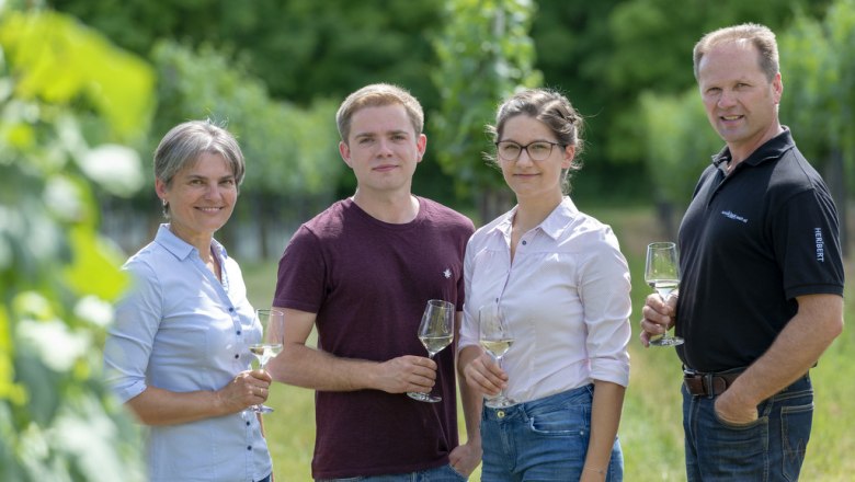 Wenzl family, © Michael Himml Four people are standing in a vineyard holding wine glasses.