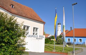 Leopold Figl Museum, © Stadtgemeinde Michelhausen Leopold Figl Museum with flags and church tower in the background.