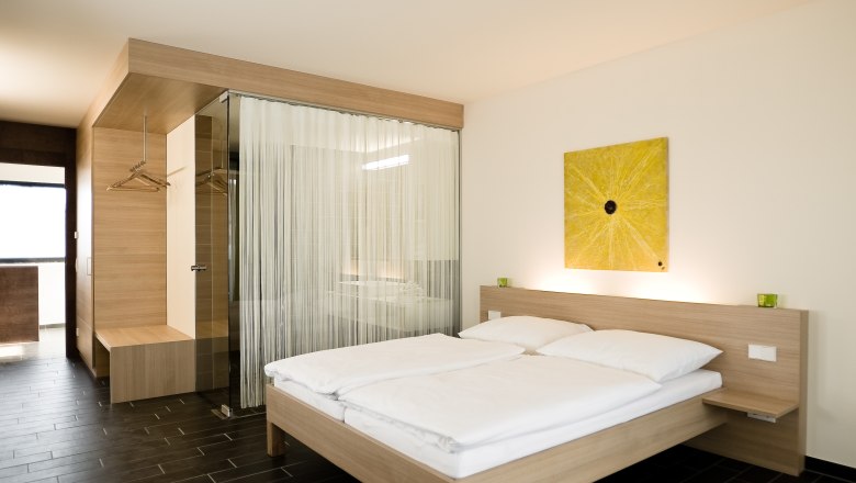 Muscat room, © Rosenberger Modern hotel room with double bed, wooden furniture and yellow artwork on the wall.