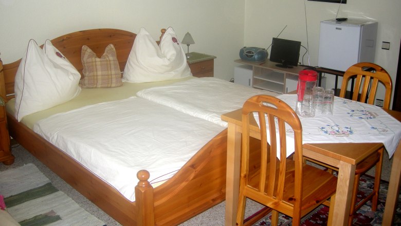 Private room Gruber, © Siegfried Gruber A cozy bedroom with wooden furniture, a double bed, a small table with chairs and a TV.