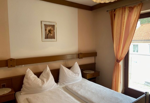 Double room, © Wiener Alpen A cozy double room with two beds, a window with a curtain and a picture on the wall.
