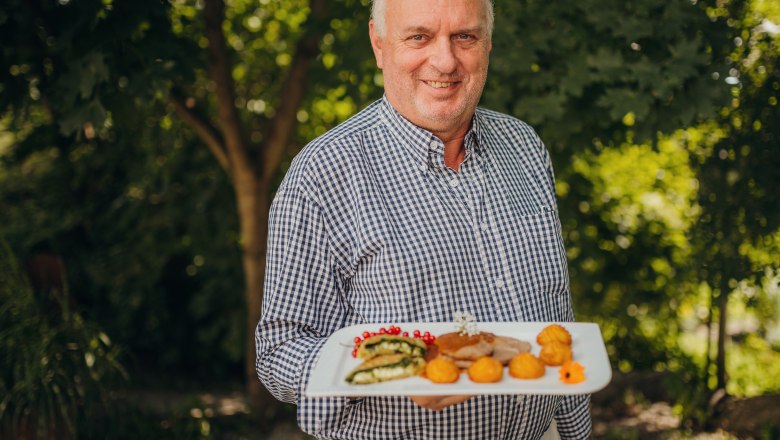Landlord Willi Falkensteiner, © Niederösterreich Werbung/Daniela Führer A man in a checkered shirt holds a plate with decoratively arranged food outside.