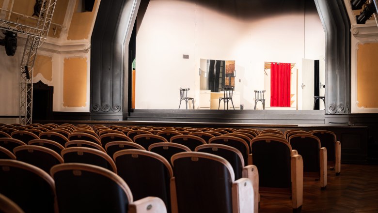 Reichenau Festival, © Österreich Werbung/Stefan Strasser Empty theater hall with a stage on which two chairs and a red curtain can be seen.