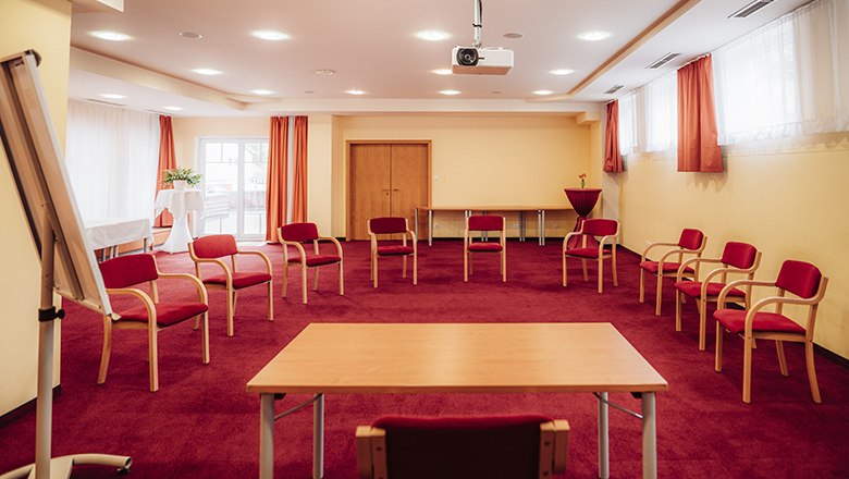 Seminar room, © Payerbacherhof - Christopher Tarkus A seminar room with a red carpet, circle of chairs, table, flipchart and projector.