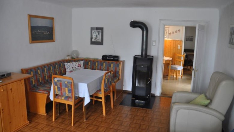 Dining area, © Familie Ackerl Cozy dining area with corner bench, table and chairs, next to a stove. In the background a passageway to another room.