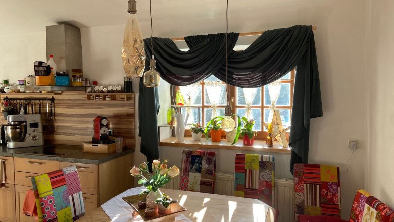 Dining area, © Wiener Alpen Dining area with wooden table, colorful chairs, plants on the windowsill and hanging lamps.