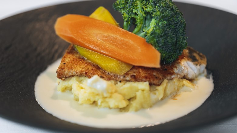 Pikeperch on mashed potatoes, © Niederösterreich Werbung/David Schreiber A dish of fried pike-perch on mashed potatoes, garnished with broccoli, carrots and yellow peppers, served on a black plate.