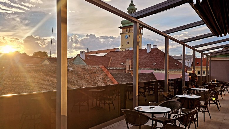 Rooftop terrace, © Rebecca Freitag Rooftop terrace with tables and chairs, view of the town hall tower and sunset.
