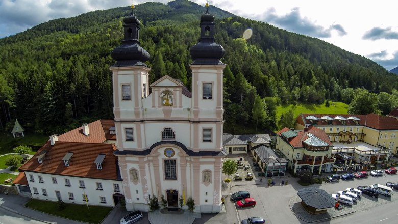 Kirchenwirt and church, © Wiener Alpen, Franz Zwickl Aerial view of a church with two towers, surrounded by buildings and forest.