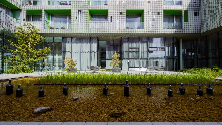 LOISIUM Langenlois, © Niederösterreich Werbung / Maximilian Pawlikowsky Modern building complex with green inner courtyard and water basin.