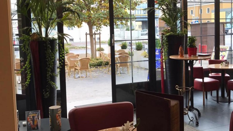 Café Stadler near the train station, © Café Stadler Interior view of a café with a view of a terrace with tables and chairs.