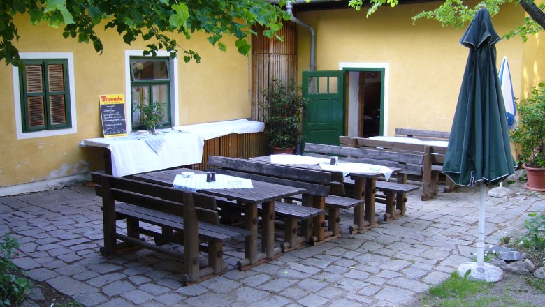 Inner courtyard of Gasthaus Perzy, © Gemeinde Haugschlag Inner courtyard of an inn with wooden benches and tables, yellow wall, green door and window, parasol and plants.